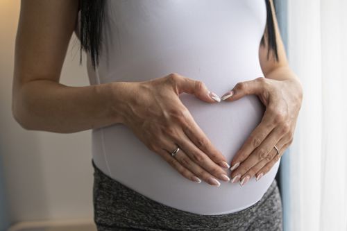Close up of pregnant woman's belly with hands making a heart - Surrogacy tax deduction concept