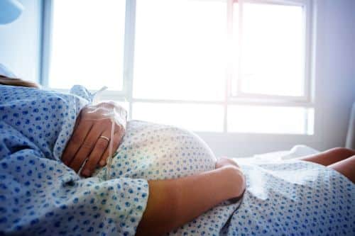Close-up of a pregnant woman's belly in the hospital bed - cost of surrogacy concept