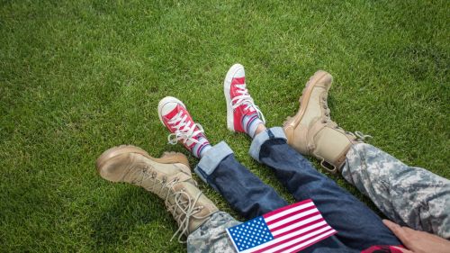 shot of the feet of a soldier sitting with their child in grass - military child support concept