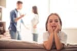 Sad little girl is looking at camera while her parents are arguing in the background - impact of divorce on children concept