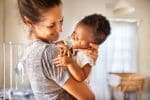 Smiling mom holding her adorable little adopted baby girl - types of adoption concept