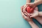 adult and child hands holding a red heart