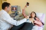Pregnant woman and her doctor in a consultation. Woman lying down while her doctor doing ultrasound examination